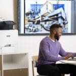 Xerox® VersaLink® C415 Multifunction Printer en situation au travail Hommes travaillant sur un ordinateur portable devant une Imprimante couleur multifonctions Xerox® VersaLink® C415